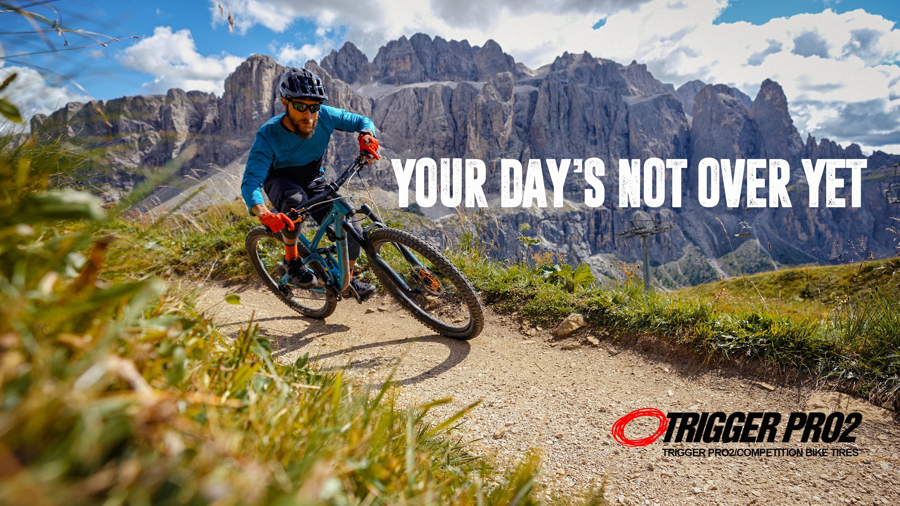 Mountain biker rides on a trail with mountains in the background.