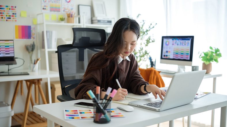 Young woman drawing at a desk in a bright room.